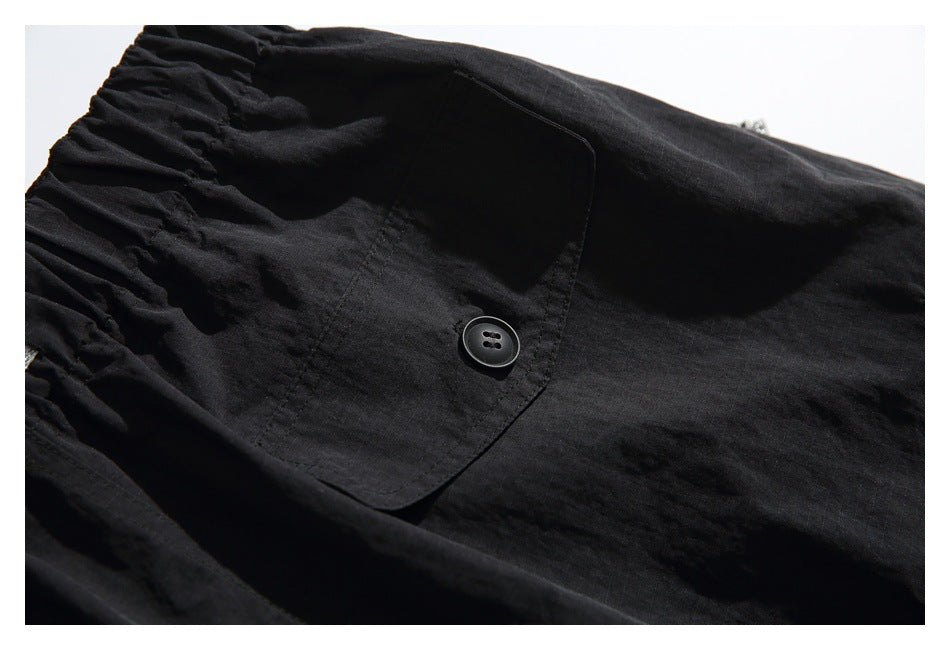 Close-up of black pants with a gathered waistband and a buttoned flap pocket.