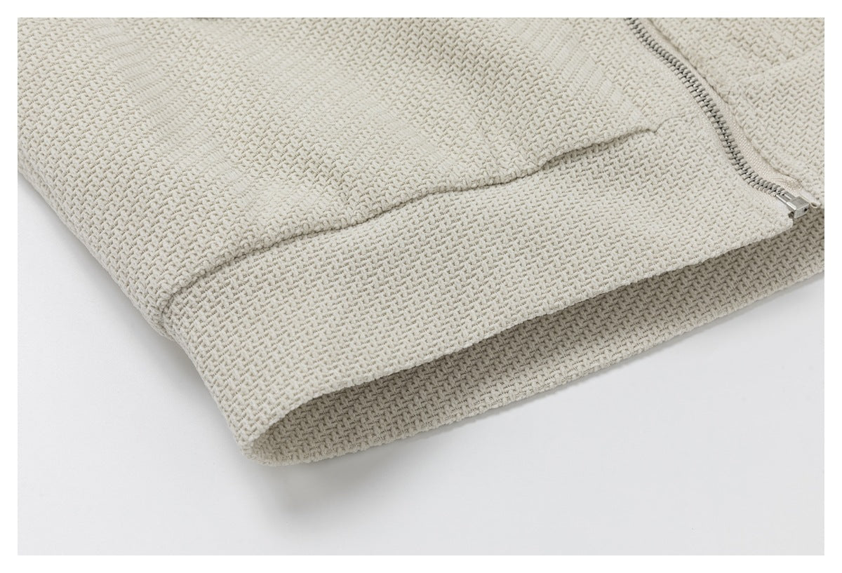 Close-up of the ivory jacket's textured hem, curved seam, and metal zipper.