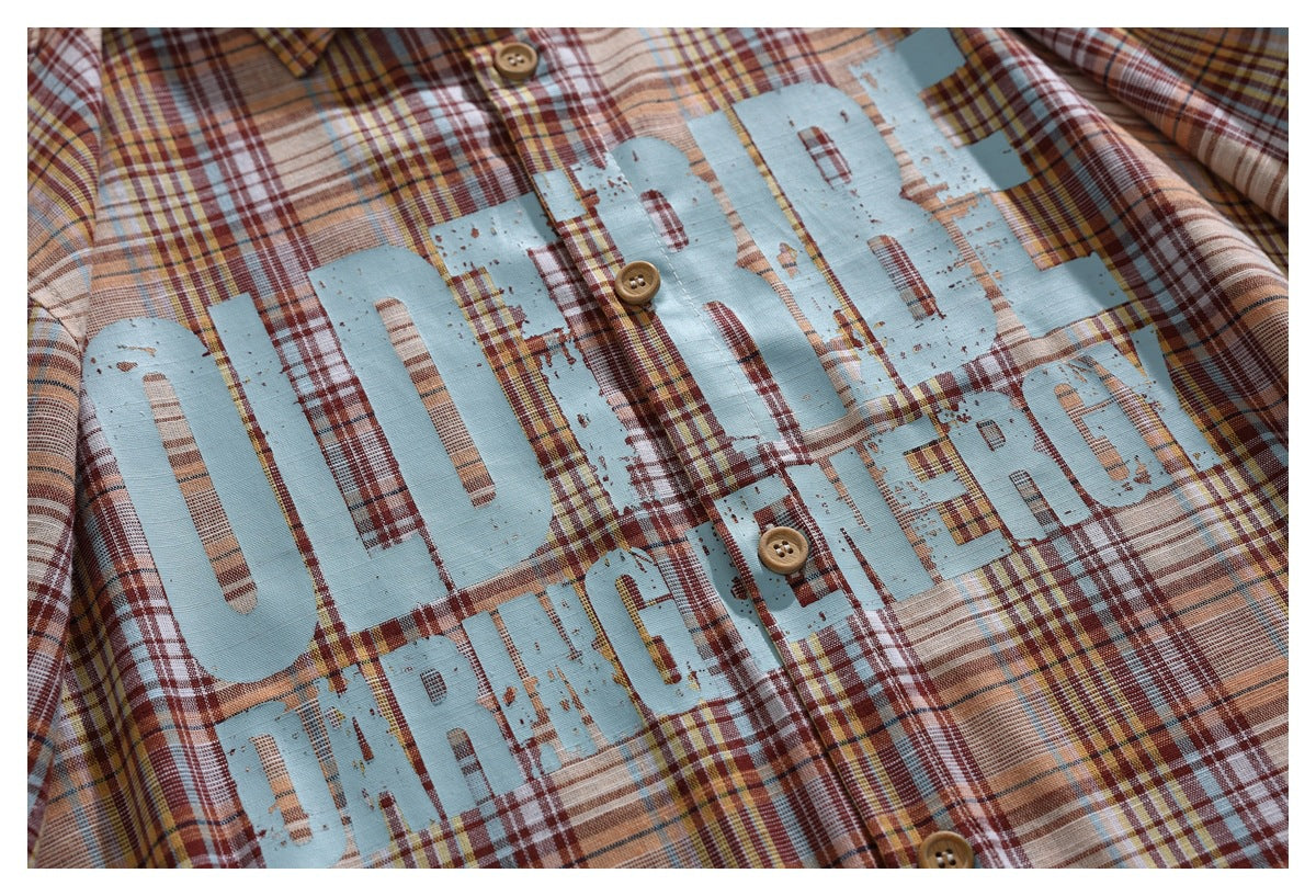 Close-up of a plaid shirt front with large distressed pale-blue lettering printed across the chest.