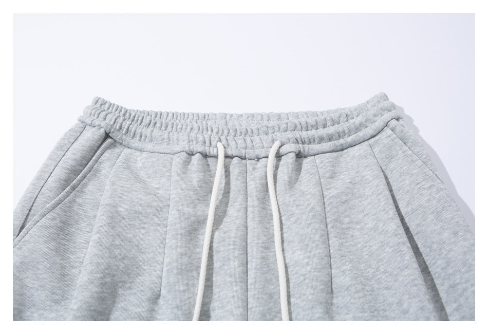 Close-up of light gray sweatpants with an elastic waistband, white drawstrings, and front pleats.