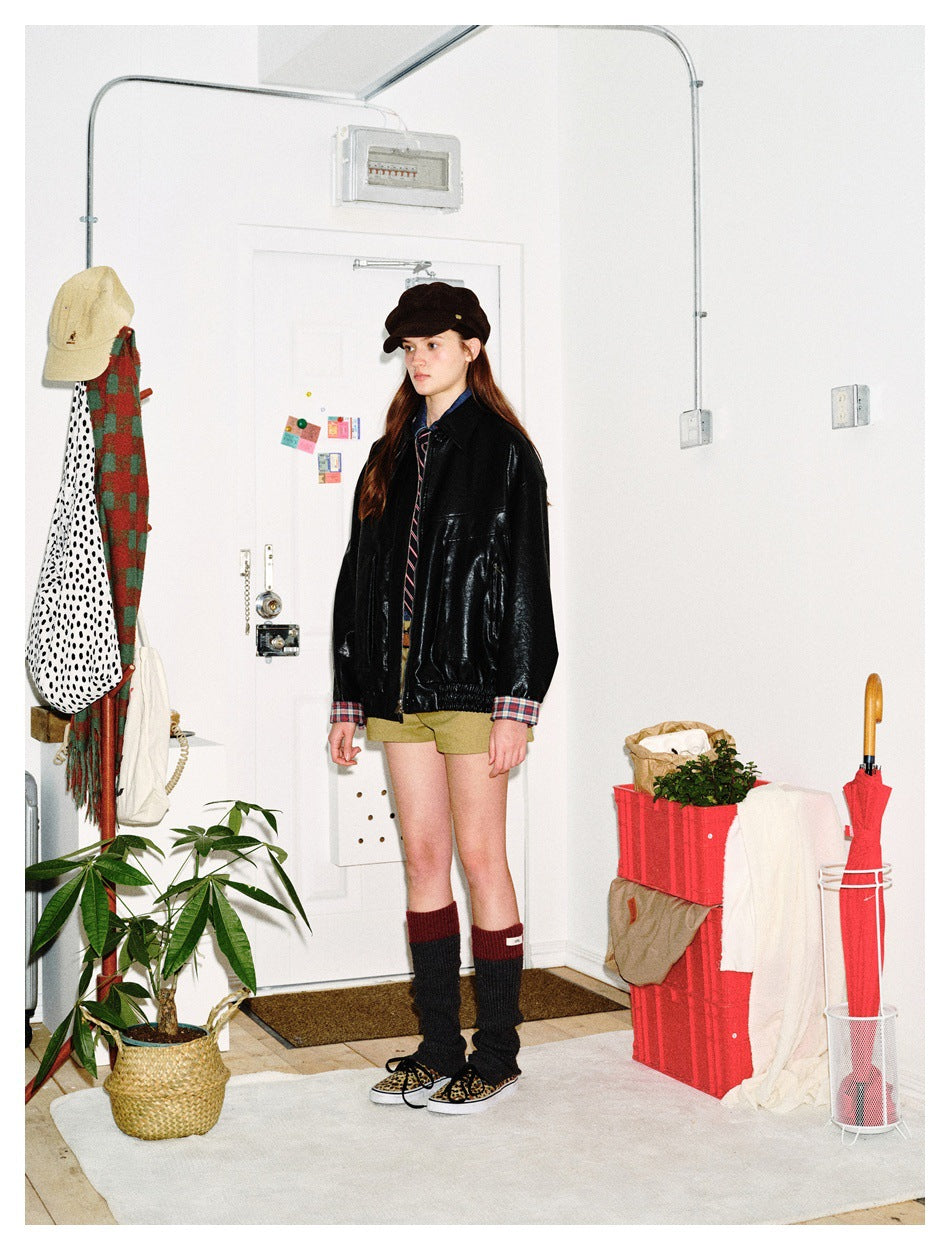 Model in a black jacket with plaid cuffs, khaki shorts and a dark cap, shown at a slight angle.