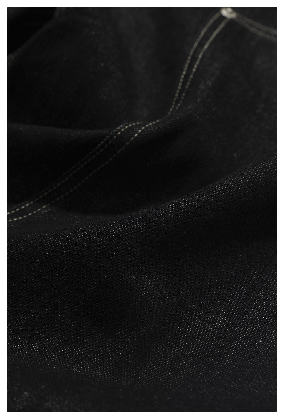 Macro view of black denim texture and pale double-stitched seams.