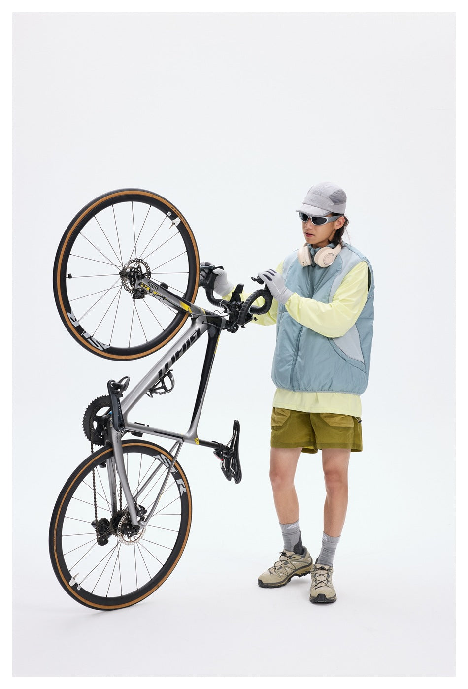 Cyclist in a pale blue zip-front vest poses beside a raised road bike.