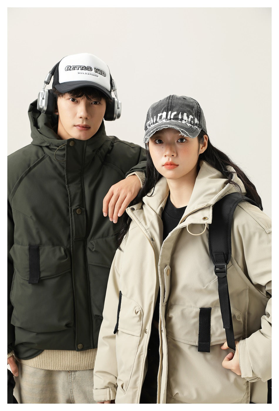 Close view of two models wearing dark olive and light beige hooded utility jackets with large front pockets.