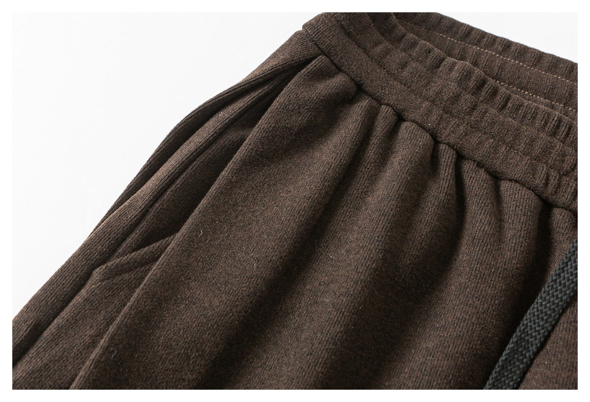Close-up of dark brown pants showing the gathered waistband, front pleats, and edge of a side pocket.