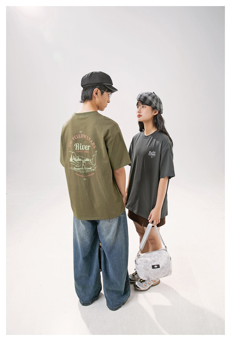 Models in olive and charcoal T-shirts, showing the olive shirt's illustrated back and the charcoal shirt's chest print.