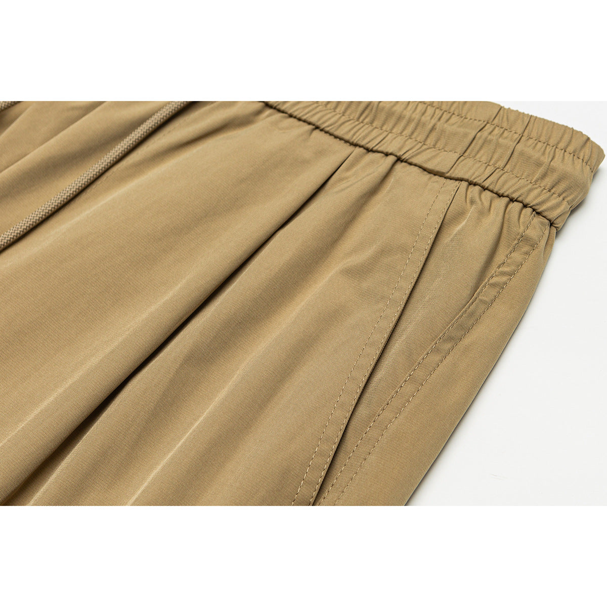 Close-up of tan pants showing the elastic waistband, drawstring, and stitched side pocket seam.