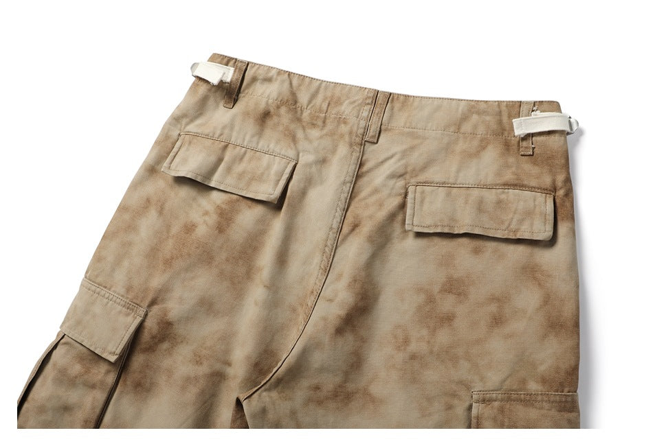 Cropped back view of tan mottled cargo pants with two flap pockets and adjustable waist tabs.