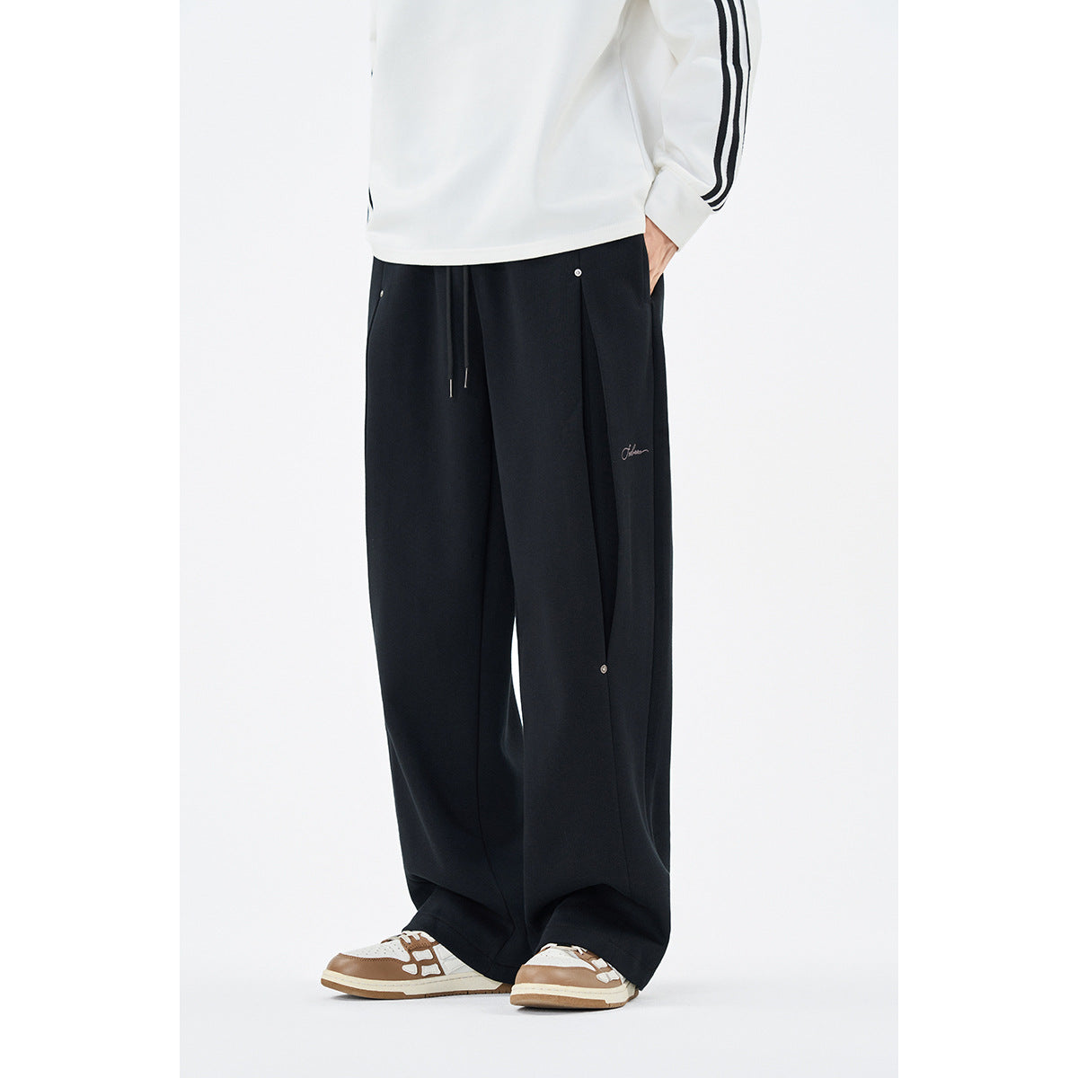 Front view of a model wearing loose black wide-leg pants with a drawstring waist and small metal details.