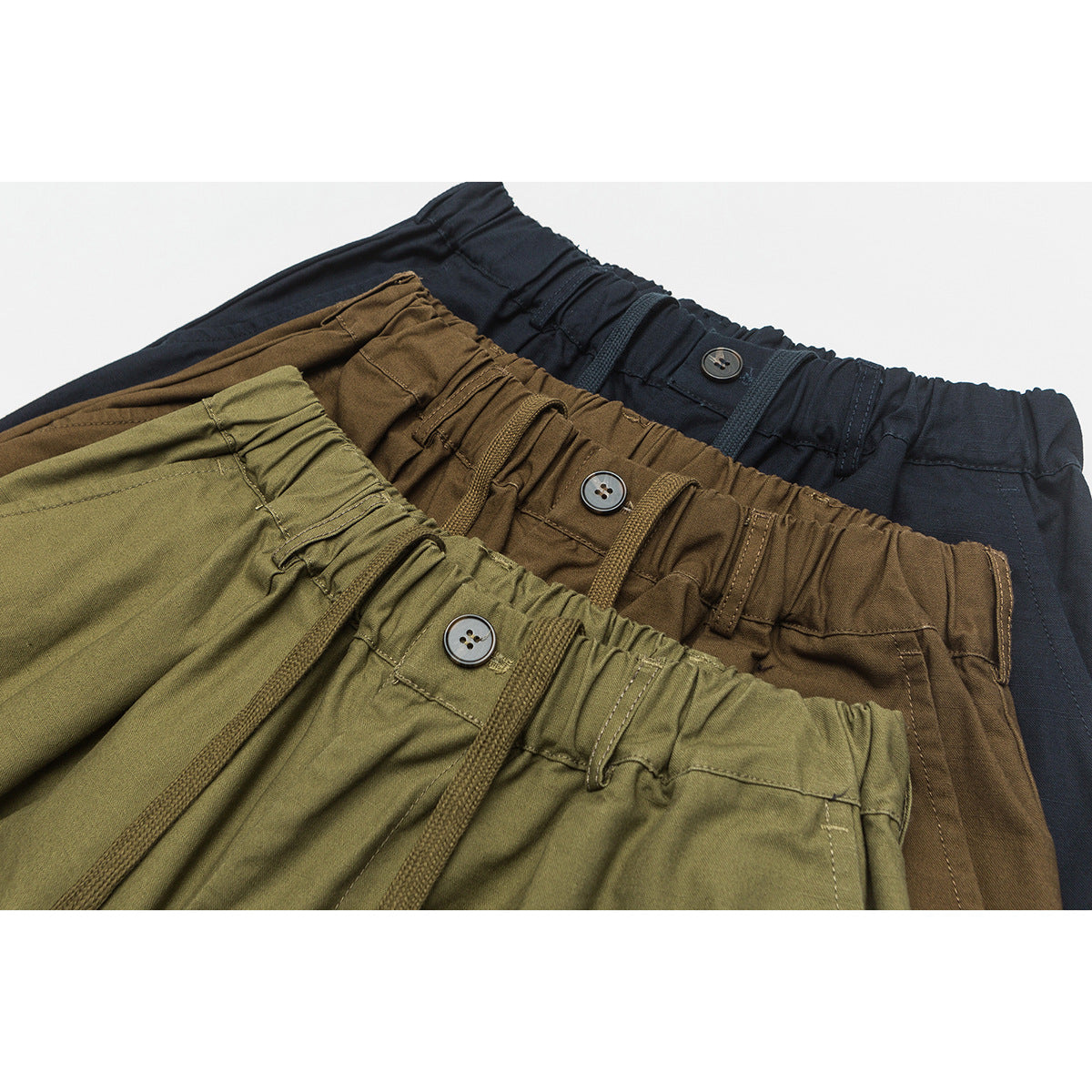 Close-up of elastic waistbands, drawstrings and buttons on olive, brown and navy pants.