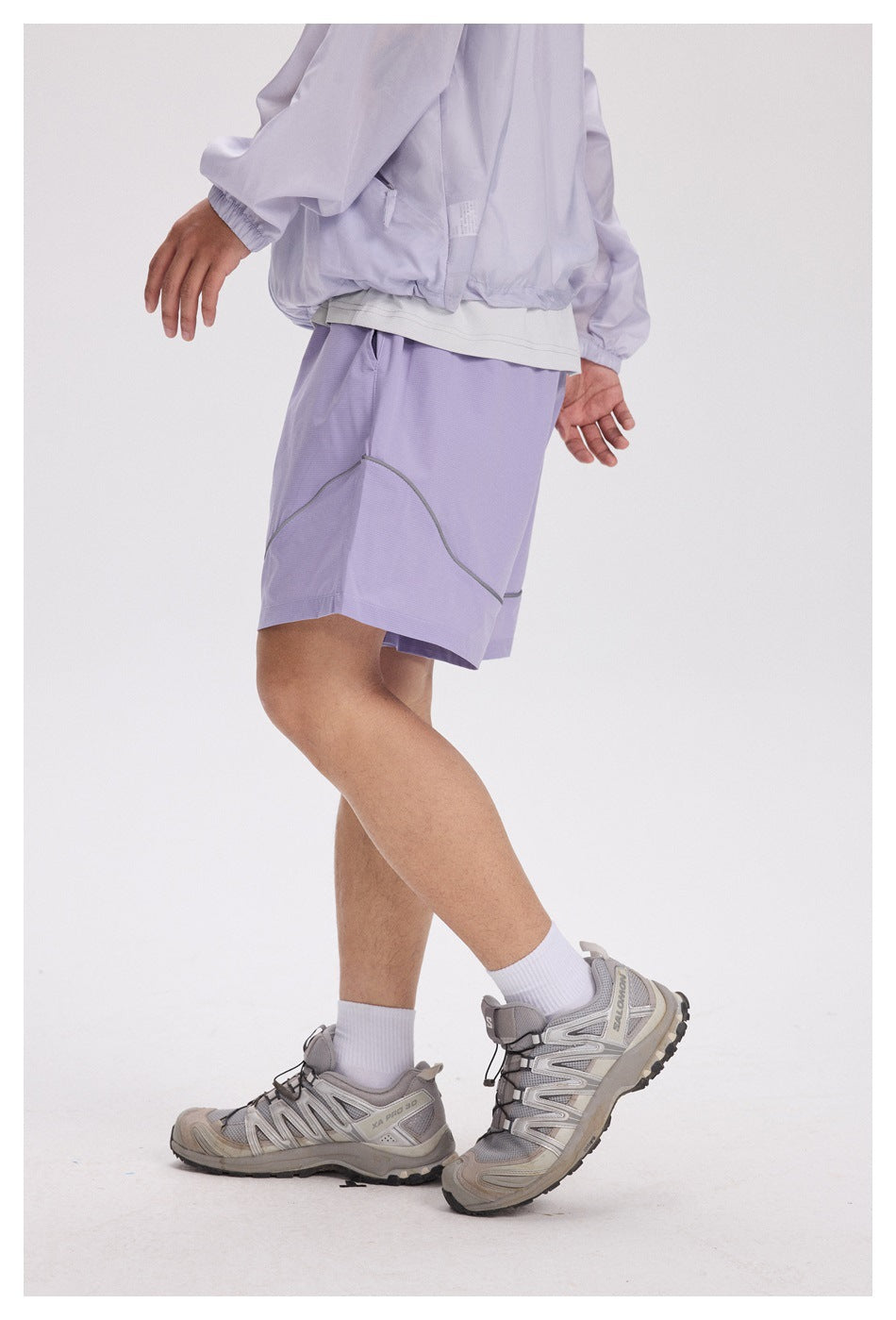 Side view of a person wearing lavender shorts with curved gray piping.