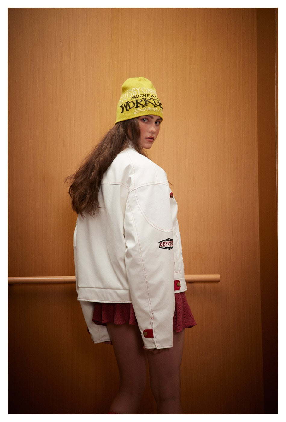 Model in a white jacket and burgundy skirt, turned to show the jacket's back and side.