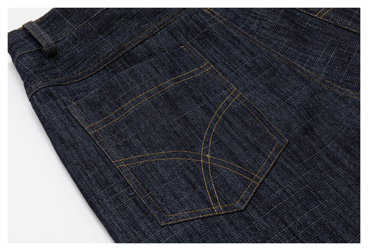 Close-up of dark indigo jeans showing a back pocket with curved golden stitching.