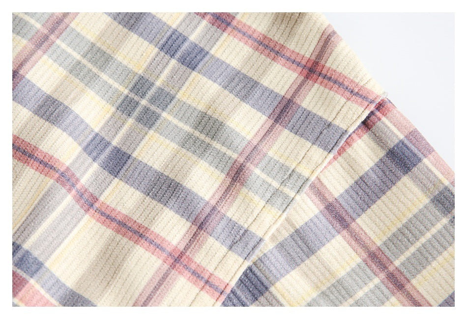 Close-up of cream plaid fabric with muted gray, blue, pink, and yellow stripes and a visible seam.