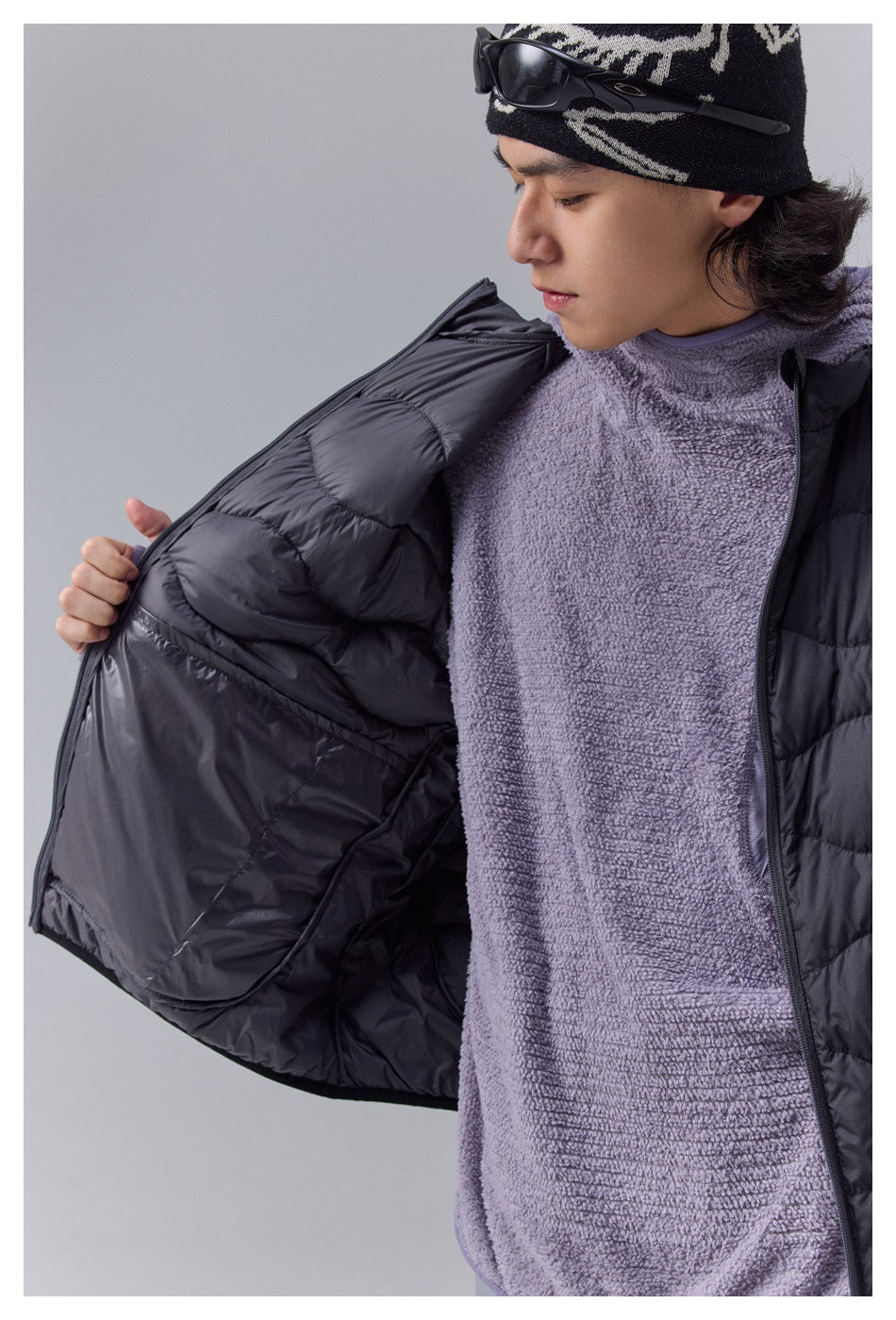 Close-up of a model opening a black quilted vest to show its dark lining over a lavender fleece top.