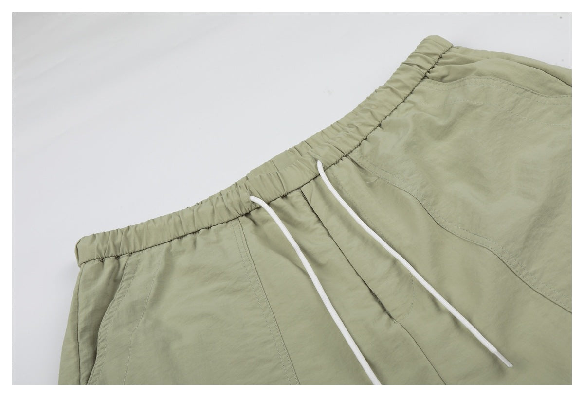 Close-up of sage-green shorts with an elastic waistband, white drawstrings and curved pocket seams.