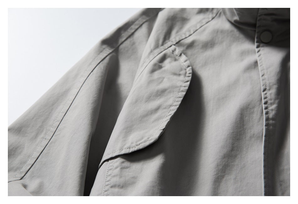 Close-up of a gray jacket’s curved flap pocket and stitched sleeve and front-panel seams.