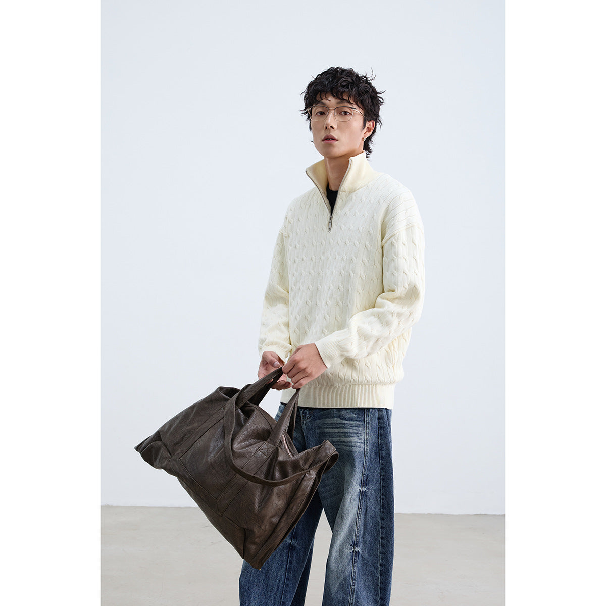 Model wearing an ivory cable-knit quarter-zip sweater with blue jeans, holding a dark brown bag.