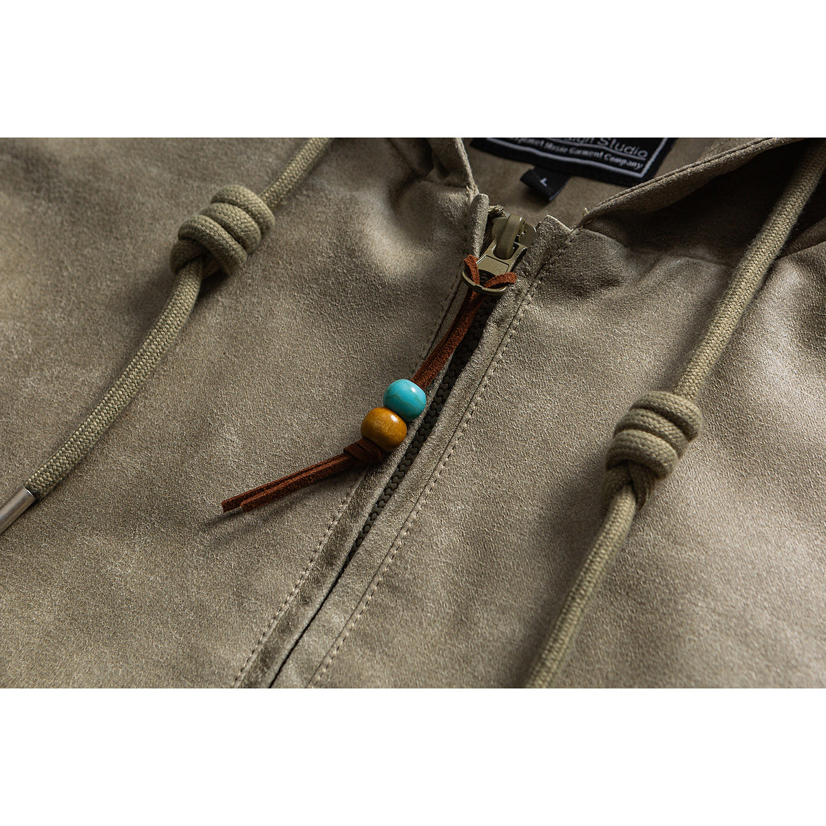 Close-up of an olive-gray hooded jacket with a front zipper, rope drawcords, and colorful bead zipper pull.