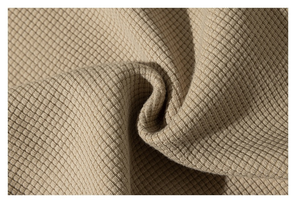 Close-up of beige fabric with a raised waffle-grid texture, gathered into soft folds.