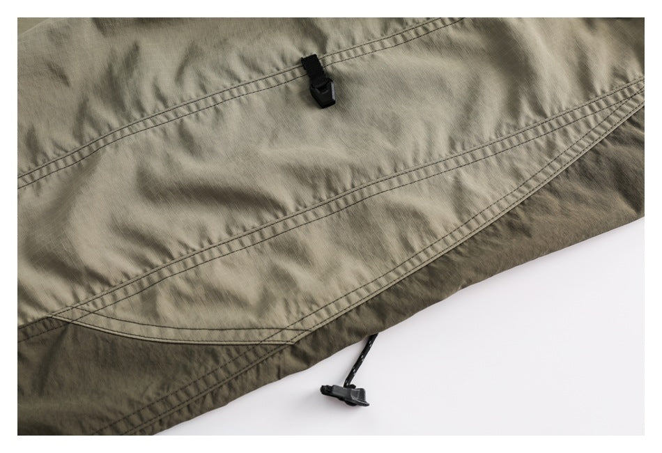 Close-up of olive fabric with curved double stitching and black cord toggles.