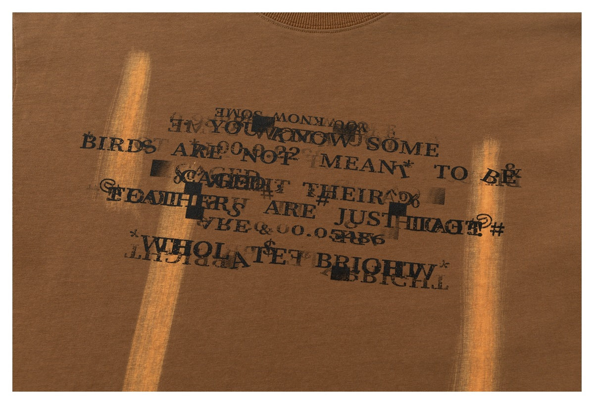 Close-up of a brown T-shirt with overlapping black English text in a distressed graphic print.