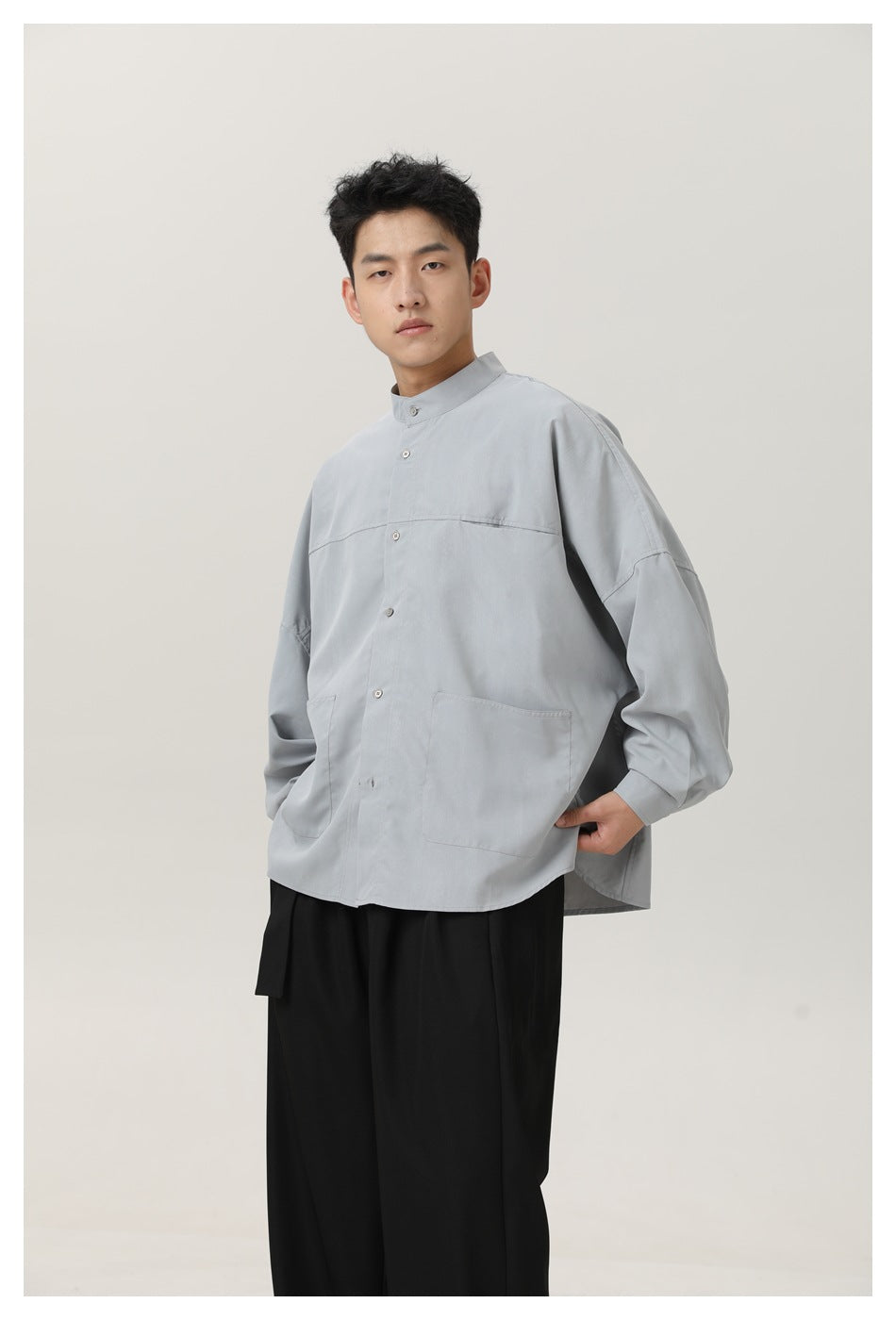Model wearing a light gray oversized stand-collar shirt with buttons, dropped sleeves, and two front patch pockets.