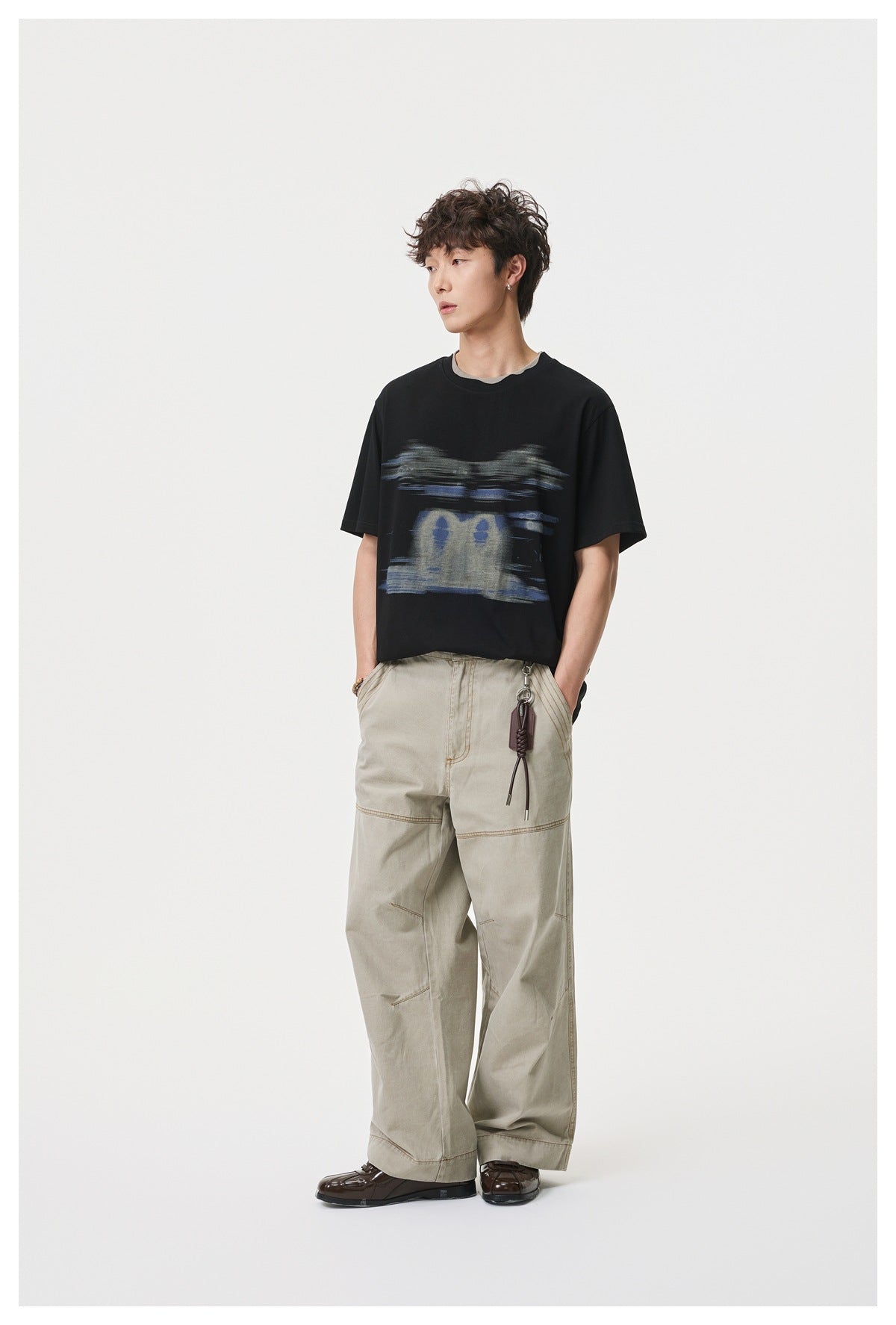 Man wearing black graphic T-shirt with gray layered collar and beige wide-leg pants, full-length standing view