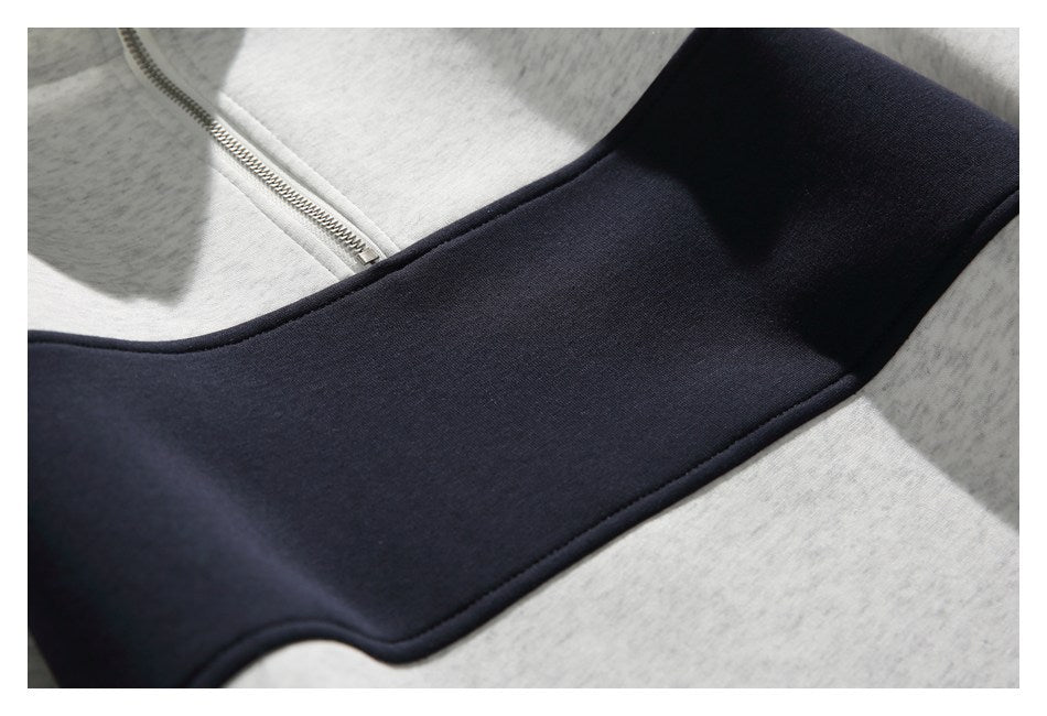 Close-up of a light gray heather sweatshirt with a broad navy panel and short silver zipper.