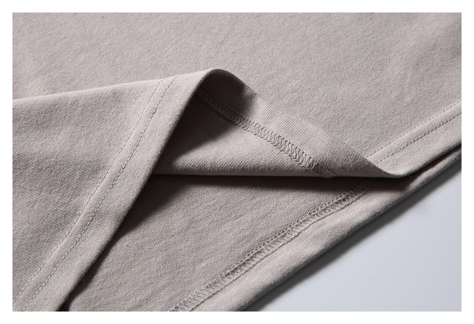 Close-up of the taupe-gray T-shirt hem, showing the folded edge and overlocked seams.