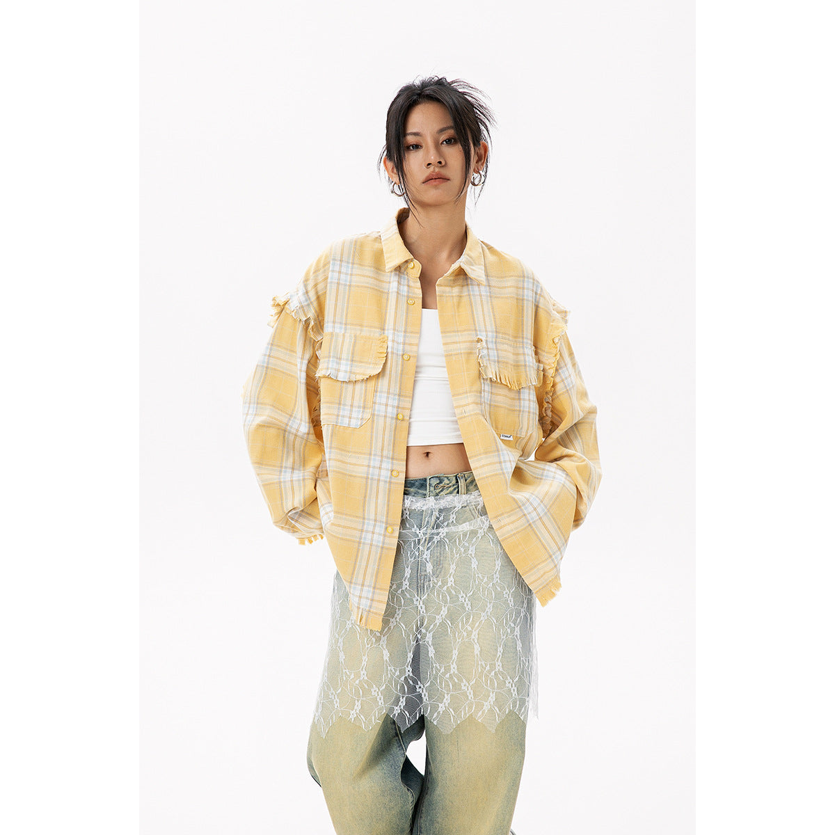 Model wearing a yellow plaid button-up with frayed ruffle details and chest pockets, over a white top and lace-layered jeans.