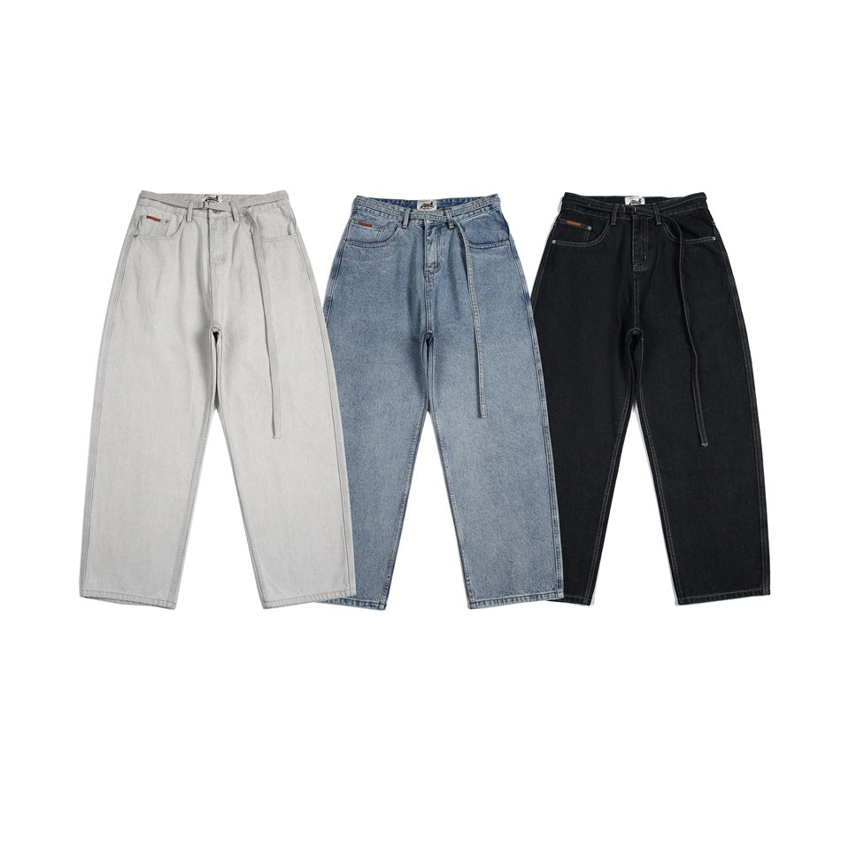 Three pairs of wide-leg jeans shown from the front in light gray, faded blue and black, each with a long belt.