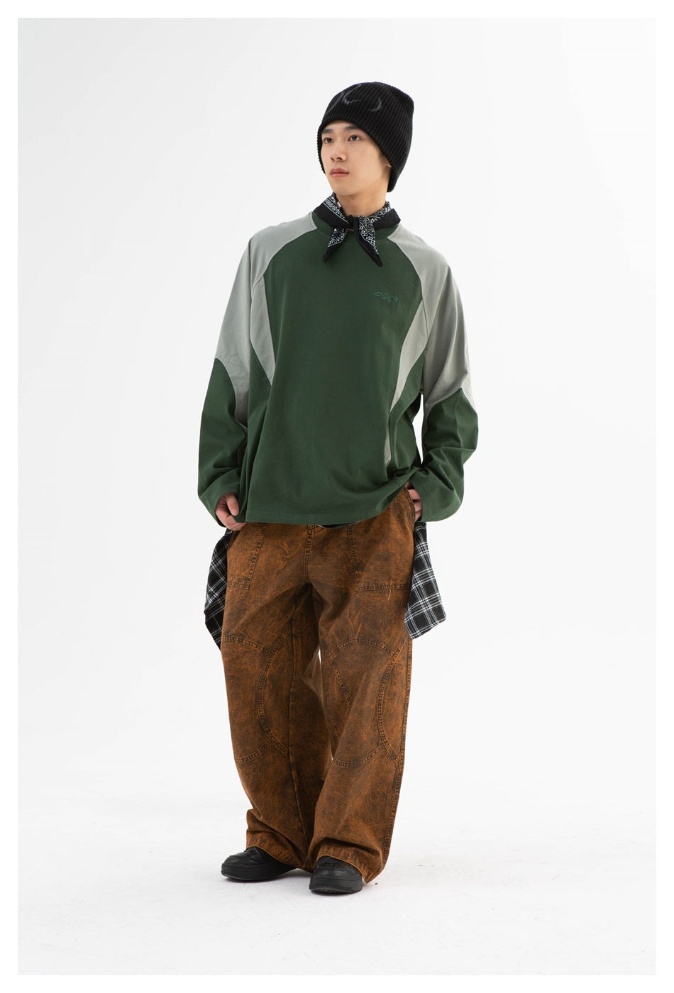 Model wearing a forest-green and pale gray raglan sweatshirt with loose brown pants and a black beanie.