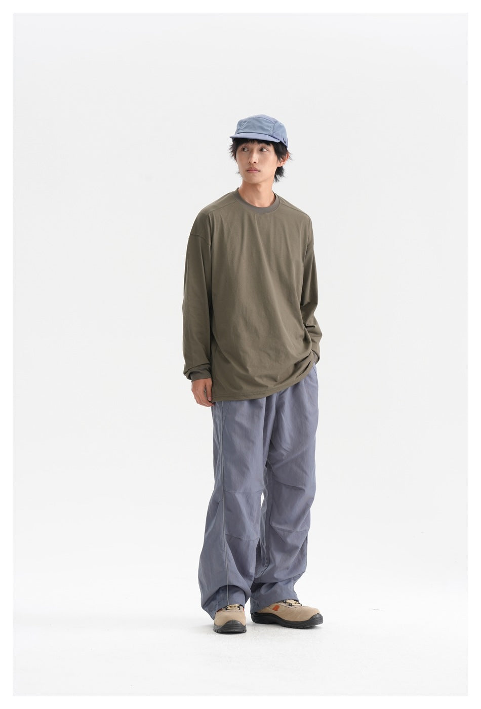 Model wearing an army green long-sleeve top with gray wide-leg pants, blue cap and beige shoes, standing front view