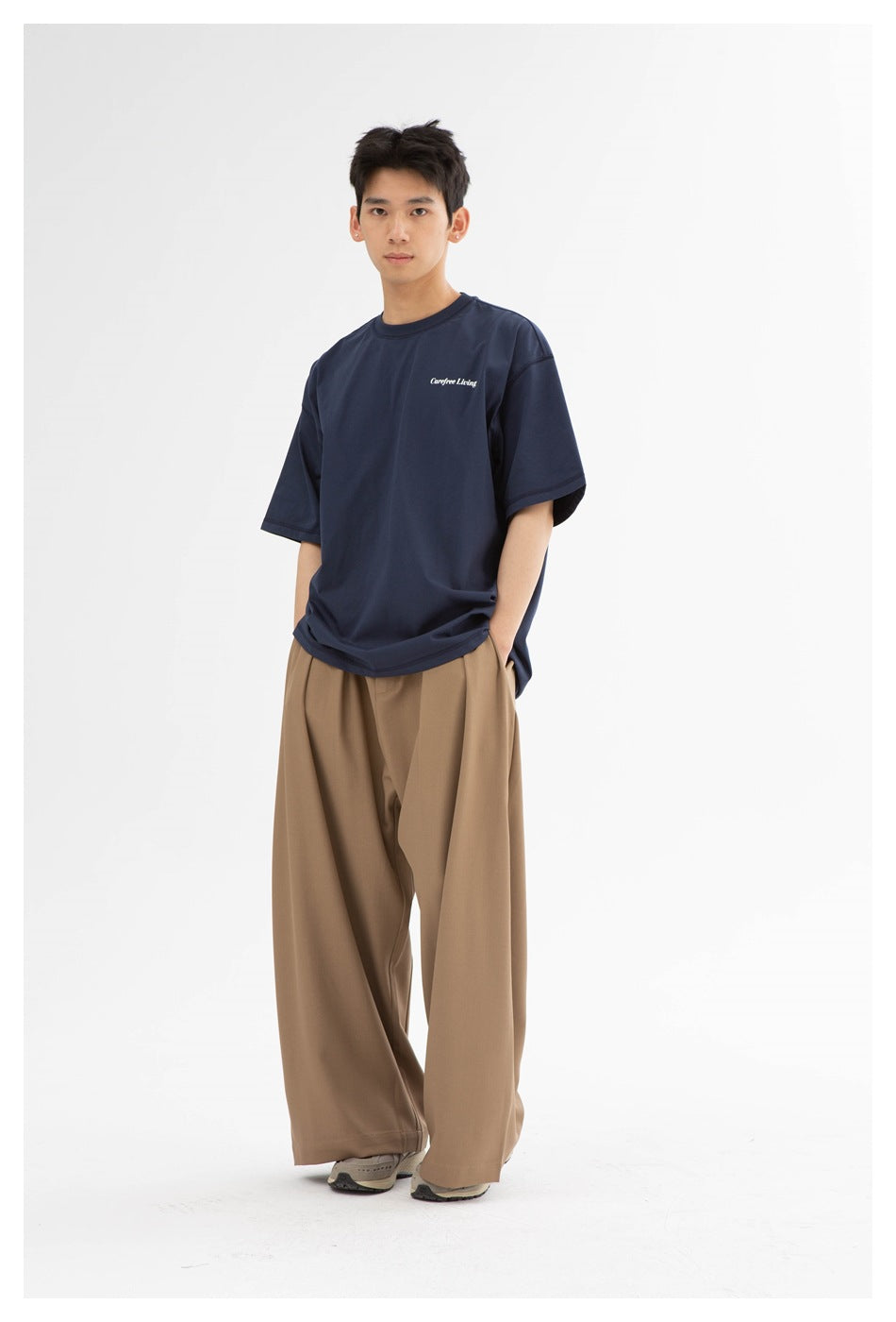 Full-length front view of a model wearing a navy T-shirt with a small chest print and wide-leg tan trousers.