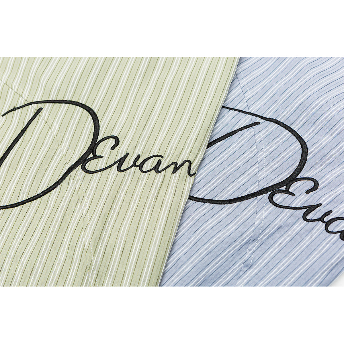 Close-up of black cursive embroidery on pale green and light blue striped shirt fabric.