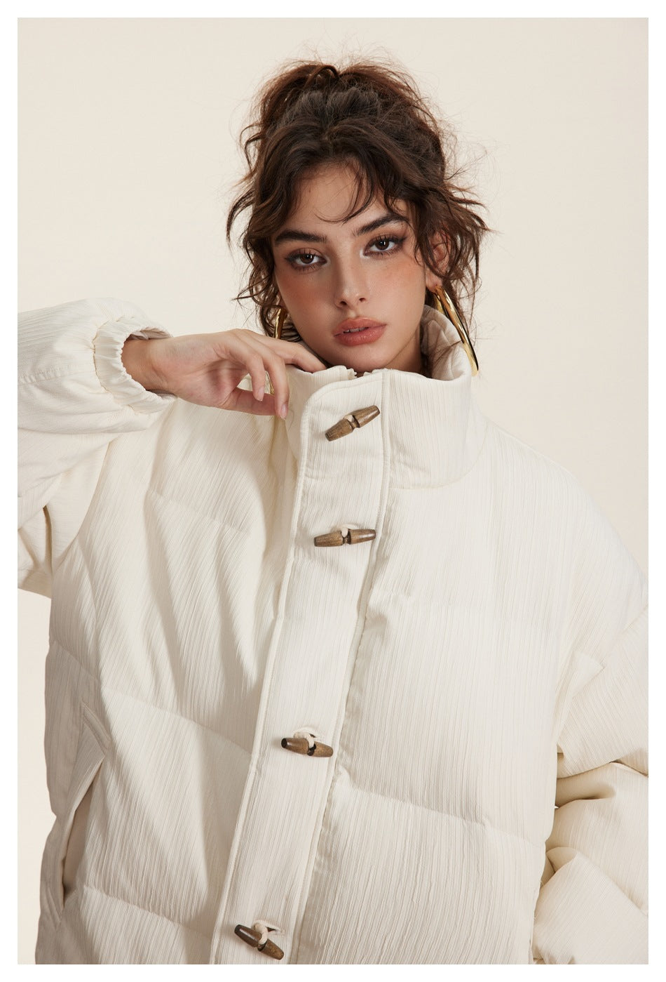 Close view of a model wearing an ivory puffer jacket, highlighting its high collar and brown toggle fasteners.