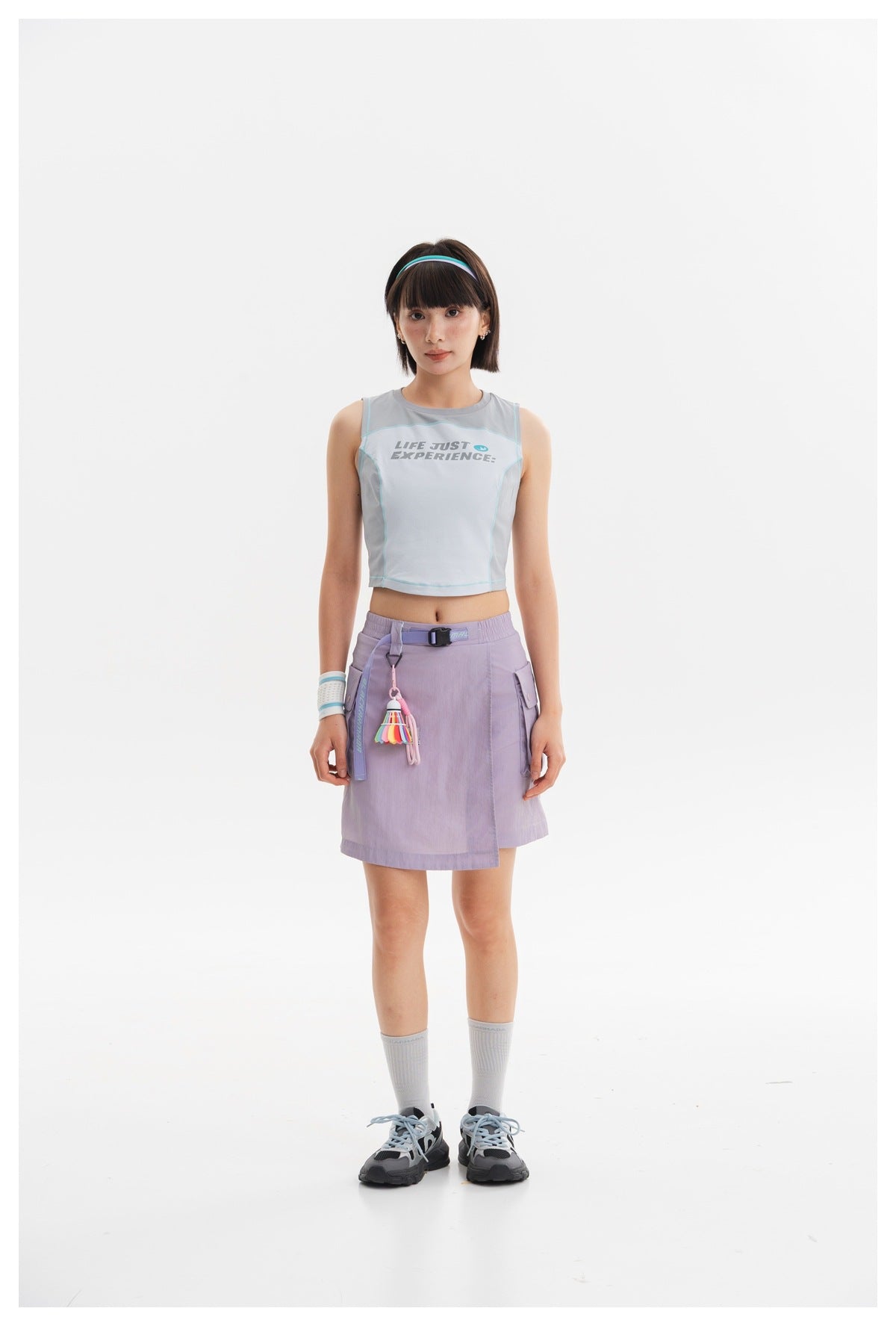 Model wearing a pale blue sleeveless crop top with turquoise trim and a lavender skirt.
