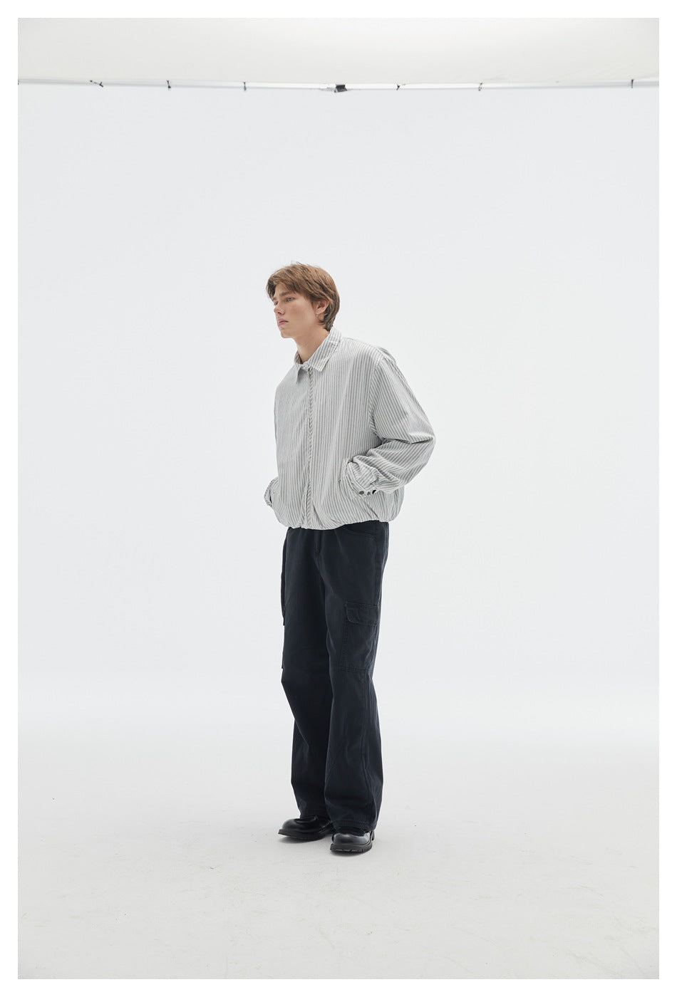 Model in a light gray pinstriped zip jacket and black cargo pants, shown at a three-quarter angle.