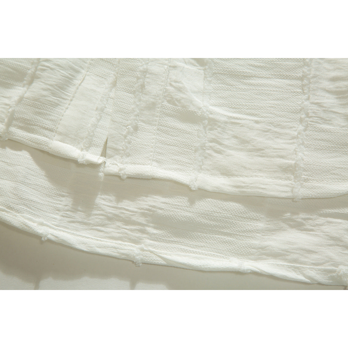 Close-up of the ivory shirt's textured panels and hem, showing raised seams and alternating woven patterns.
