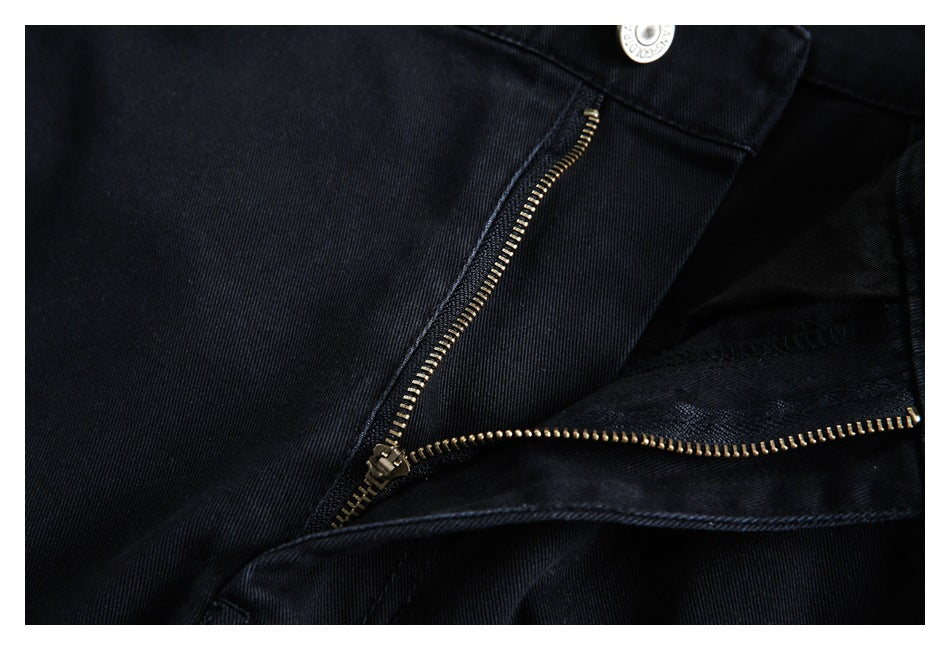 Close-up of black trousers with the fly open, showing a brass-colored zipper and silver button.