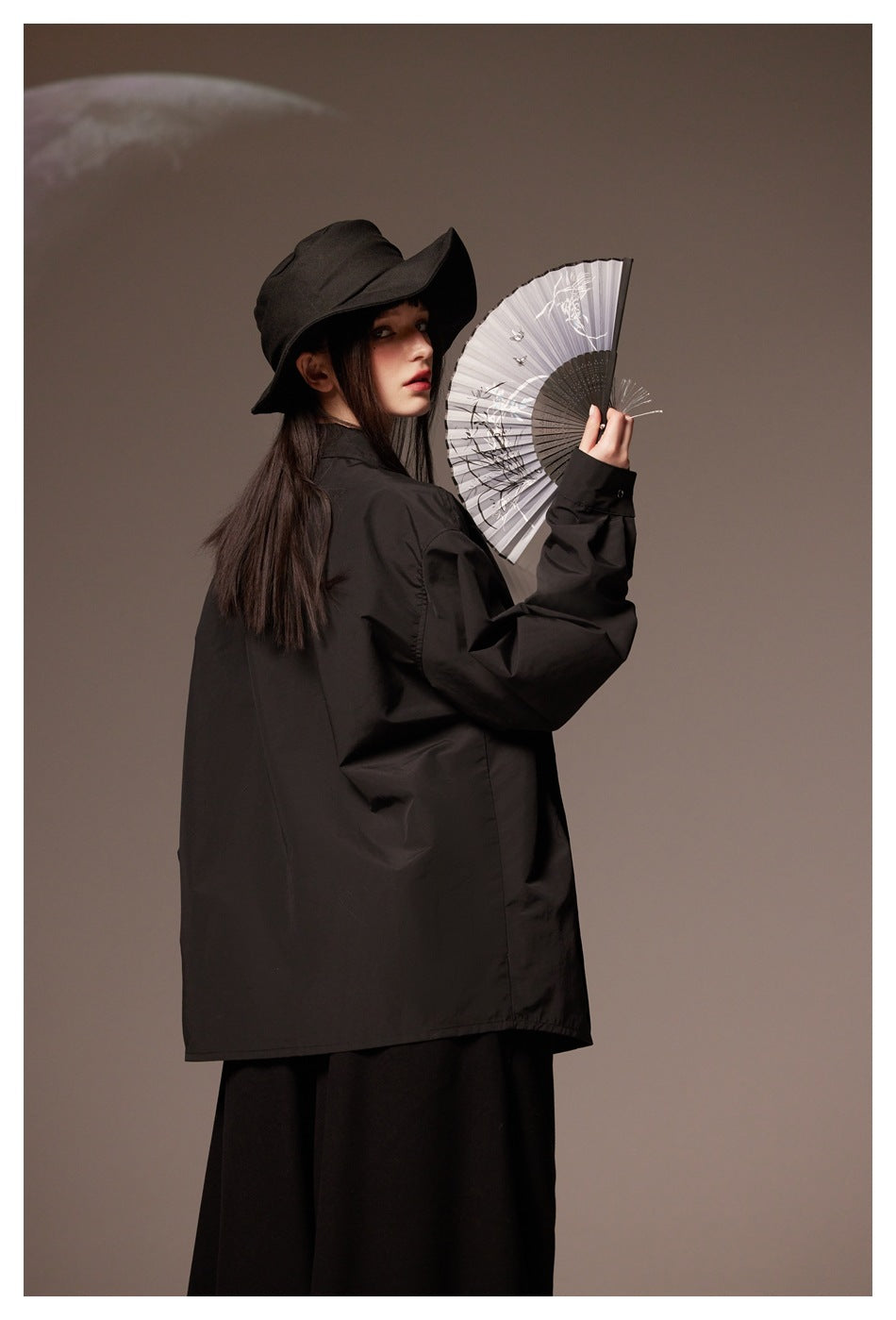 Model wearing a loose black shirt and wide-brim hat, shown from the side and back with an open fan.
