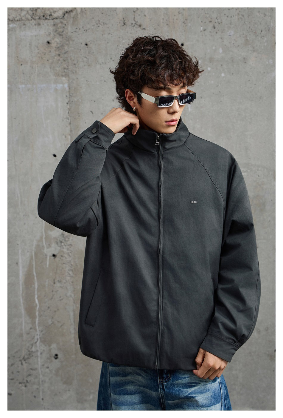 Model wearing a charcoal-gray zip jacket with a raised collar and small chest detail, shown from the front.