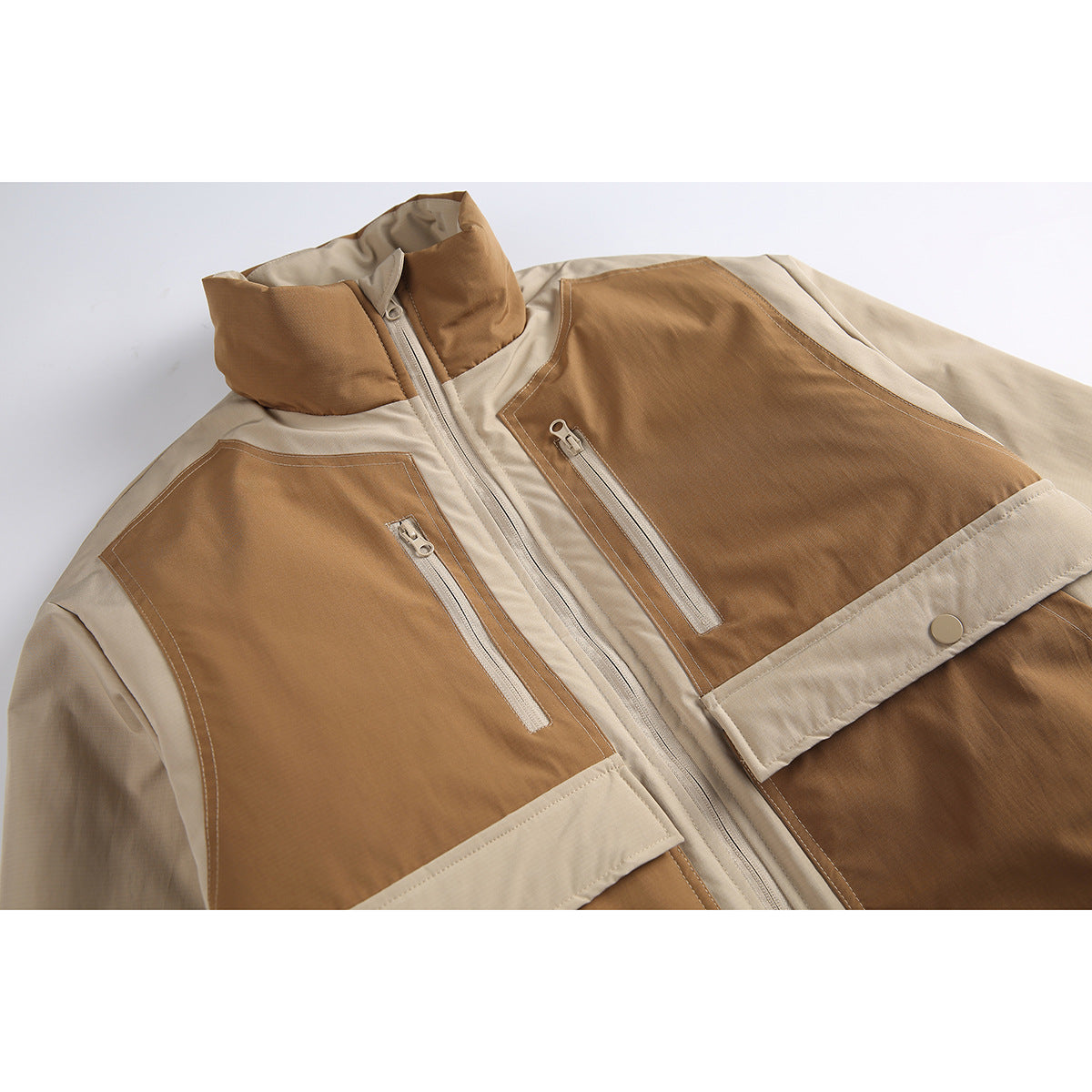 Close-up of a beige and brown color-block jacket front with a stand collar, central zipper, and zippered chest pockets.