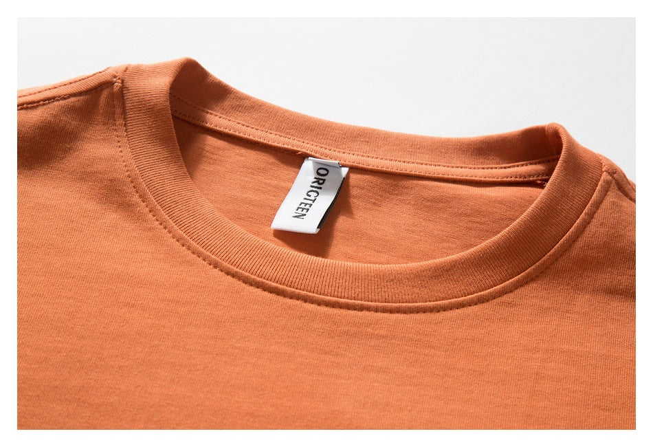 Close-up of the orange T-shirt's crew neck, ribbed collar, and ORIGTEEN label.