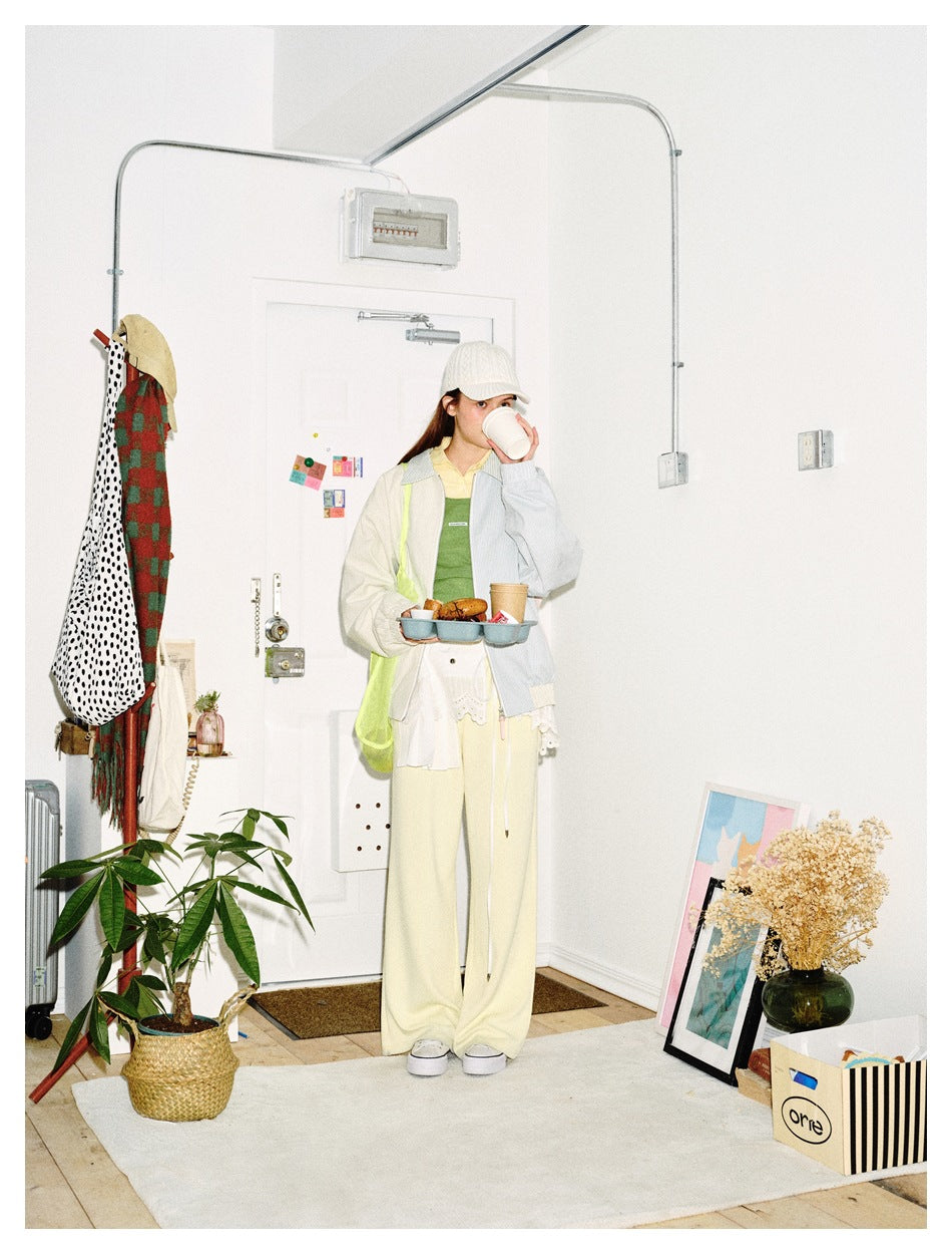 Full-length model wearing a pale blue and cream pinstriped jacket with cream trousers, holding a tray and cup.