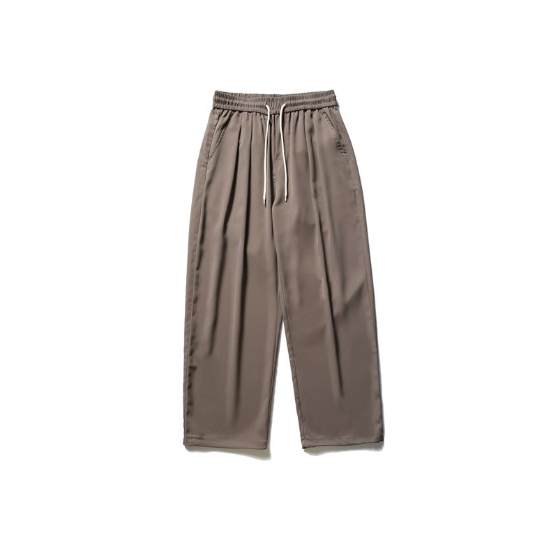 Brown wide-leg drawstring pants with elastic waist, front pleats and side pockets, flat lay on white