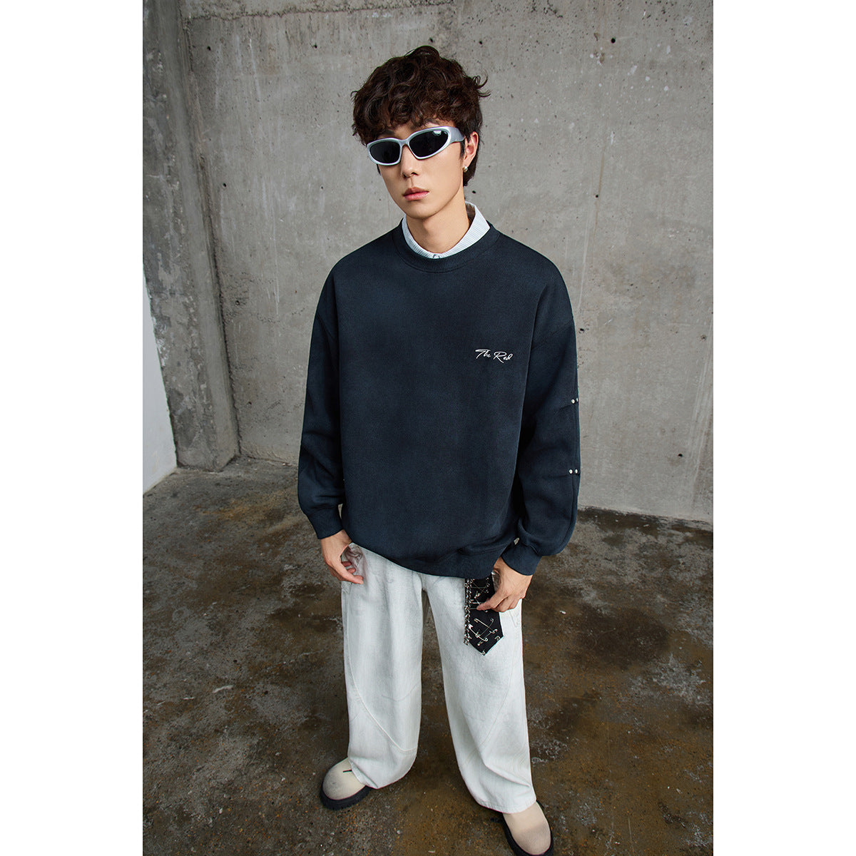 Model wearing a dark navy oversized sweatshirt with white chest script and small sleeve studs.