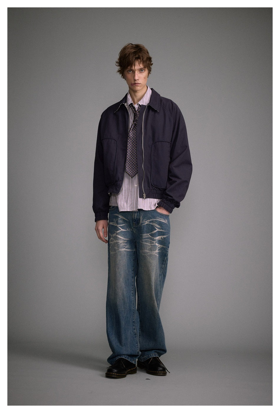 Front view of a model wearing a dark navy zip jacket with a pointed collar, large front pockets and elastic cuffs.