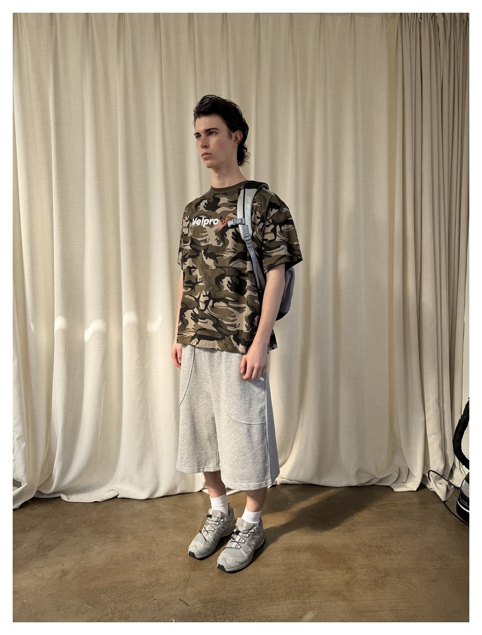 Model wearing light-gray knee-length shorts with curved pockets and a brown camouflage graphic T-shirt.